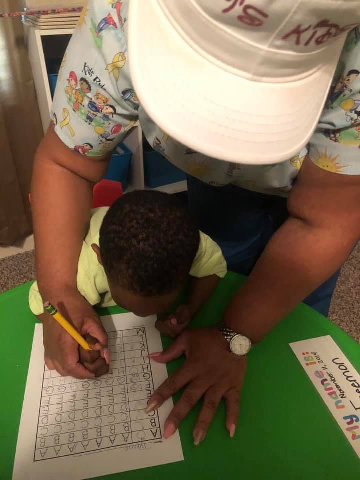 Person helping a child write on a worksheet with a pencil