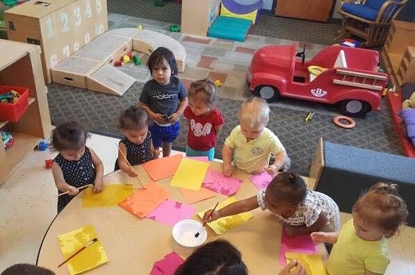 Children painting colorful paper at a table in a classroom