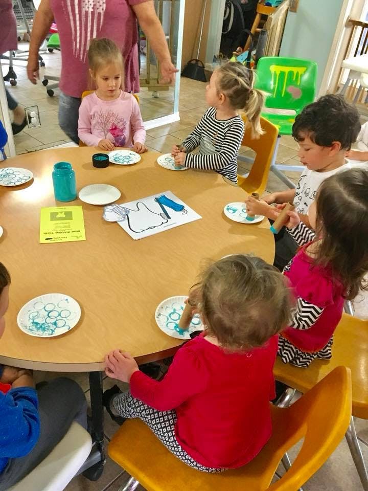 Children sitting at a table doing an art activity with paper plates