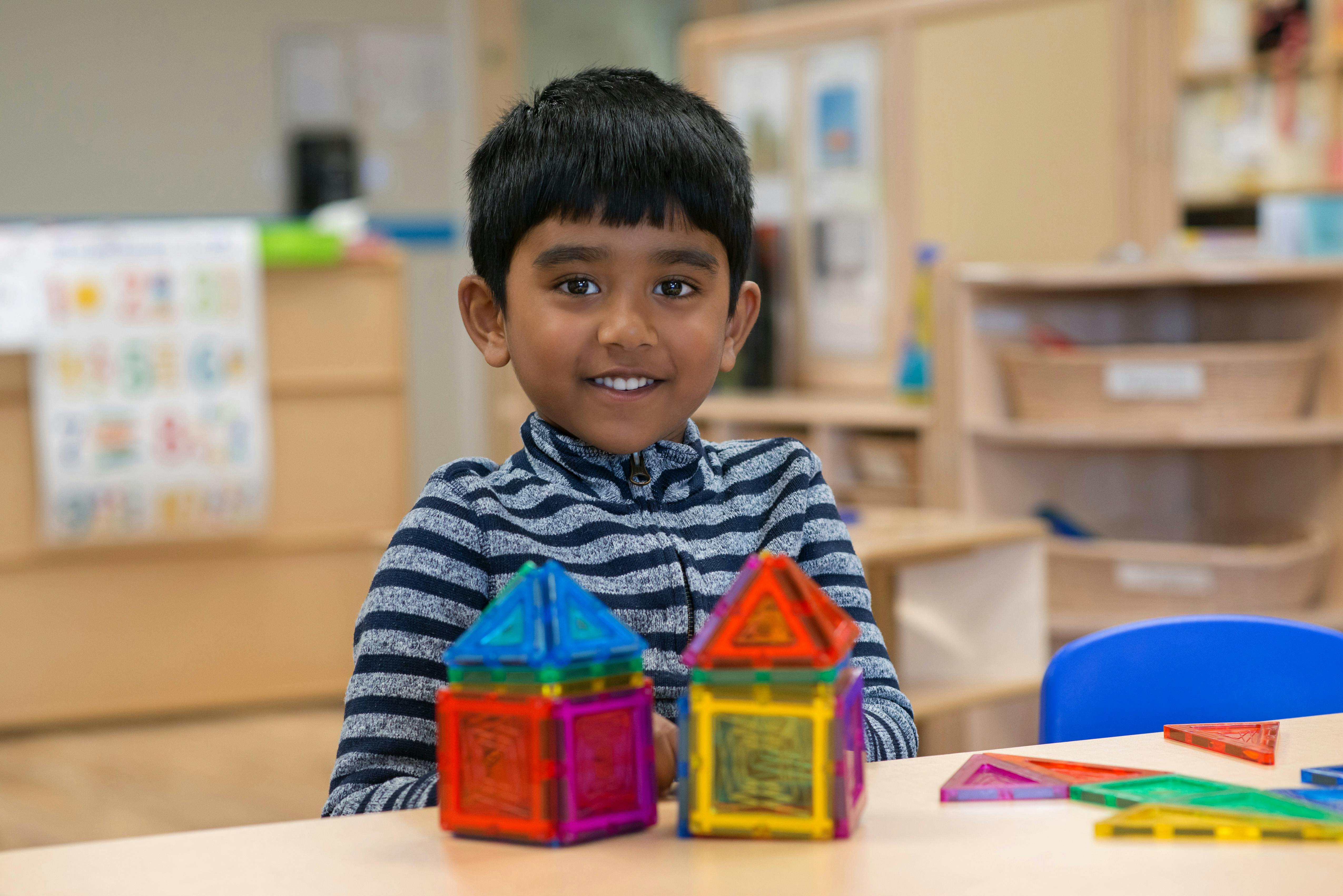 Child sitting at a table with two colorful magnetic block houses