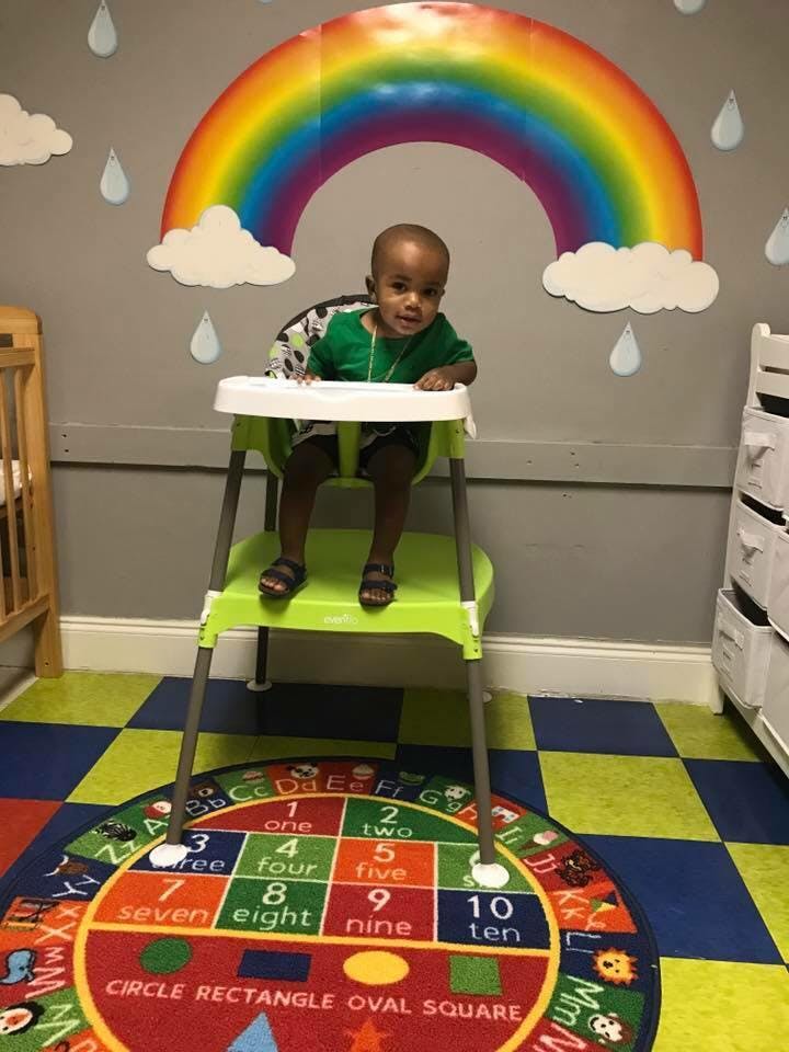 Child sitting in a high chair in a room with a rainbow wall decoration