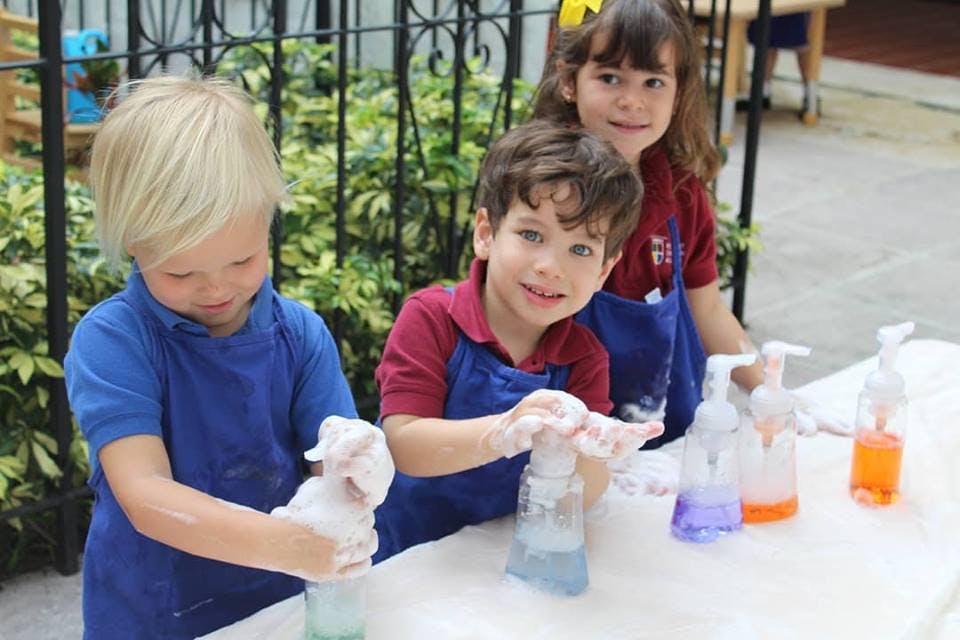 Three children washing hands with soap at a table