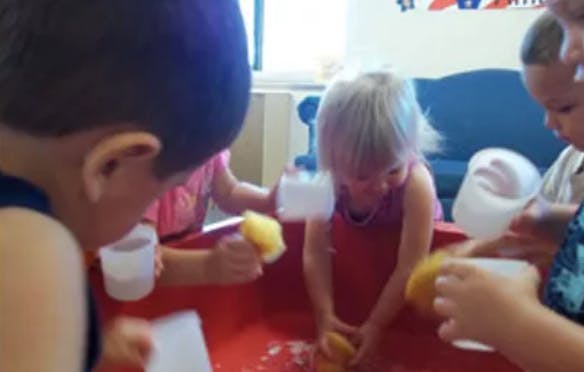 Children playing with sponges and water in a red bin
