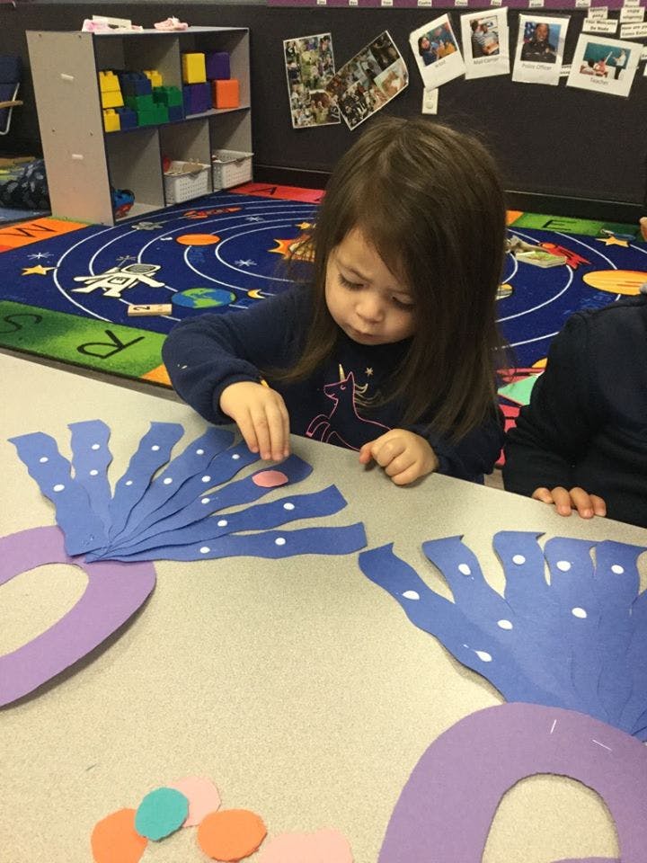 Child placing a small pink circle on a blue paper cutout