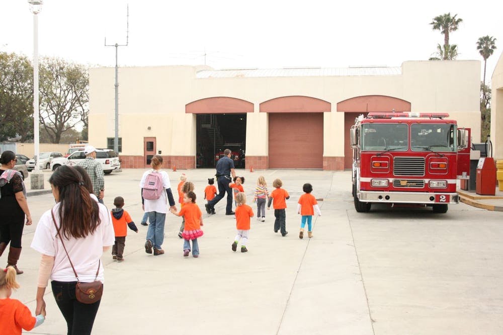 Adults and children walking towards a fire station with a fire truck