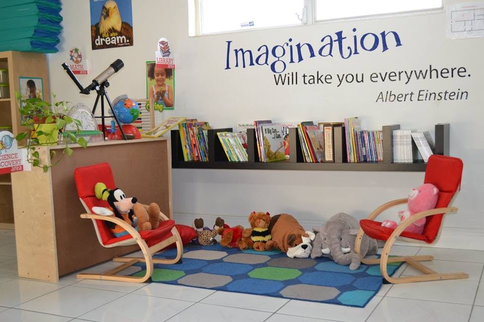 Children's reading nook with two red chairs, stuffed animals, and books