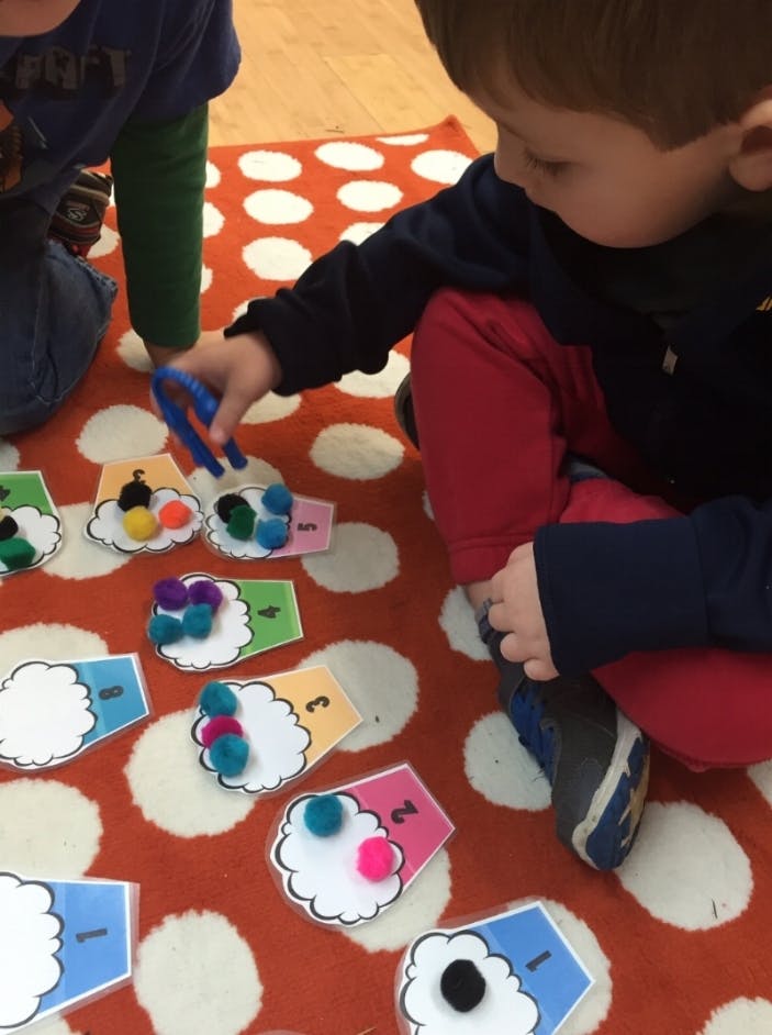 Child playing with pom-poms and numbered cards on a rug
