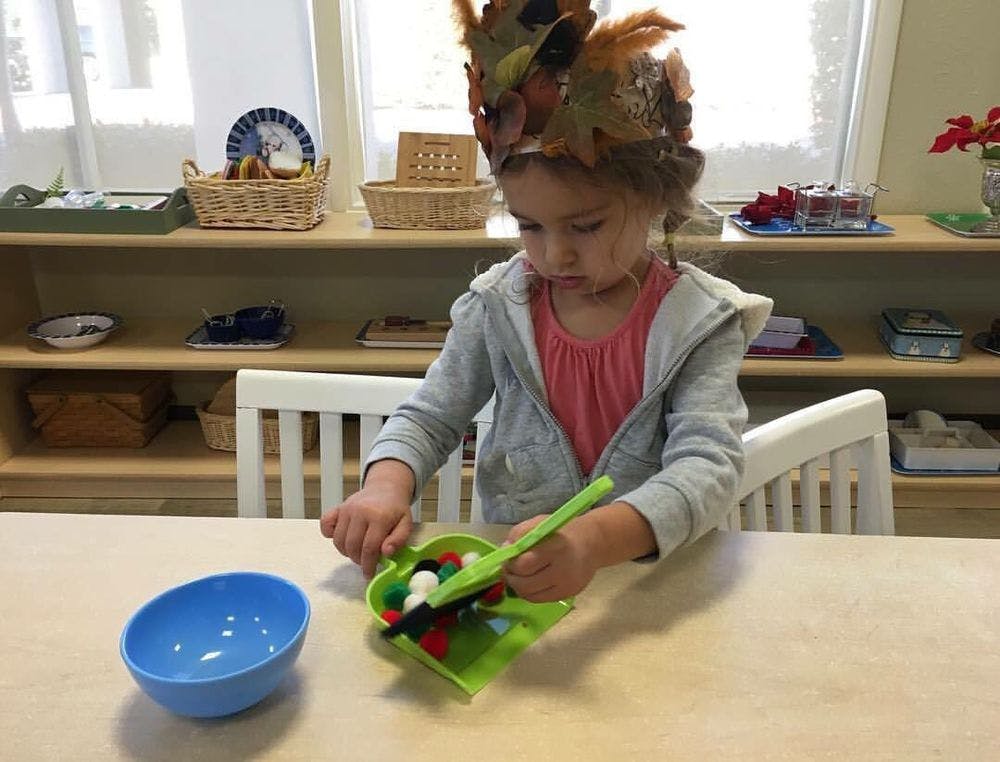 Child wearing a leaf crown playing with a scoop and small objects