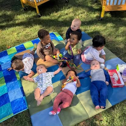 Group of infants sitting and lying on a mat on the grass