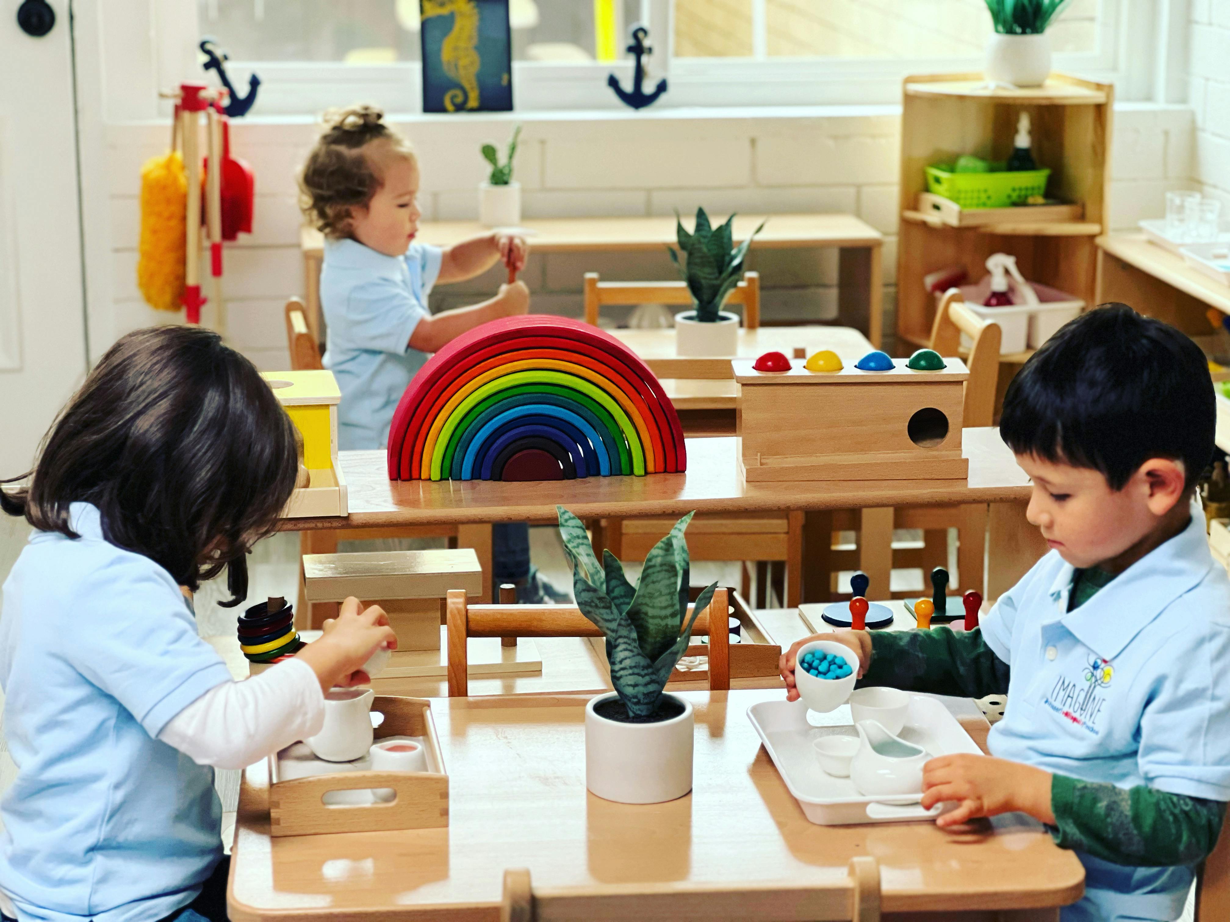 Three children playing with toys at small tables in a classroom