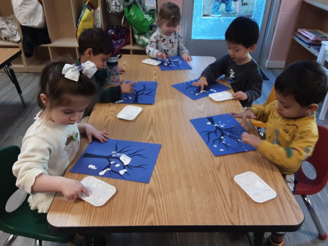 Children finger painting tree branches with white paint on blue paper