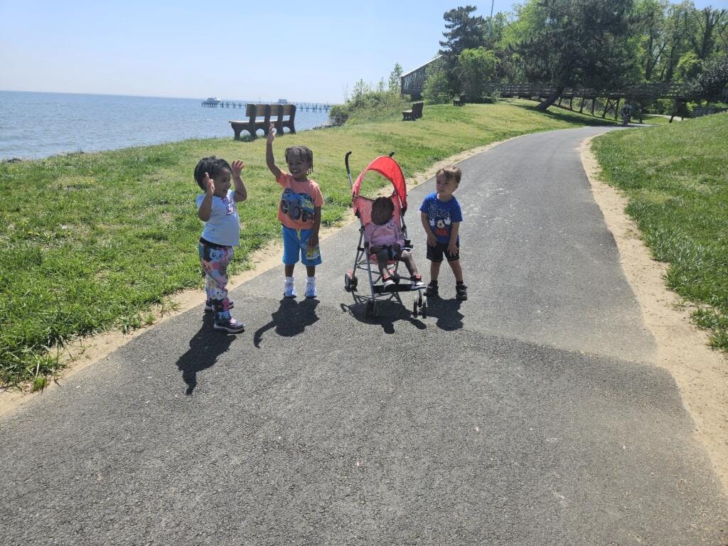 Three children and a baby in a stroller on a paved path near water