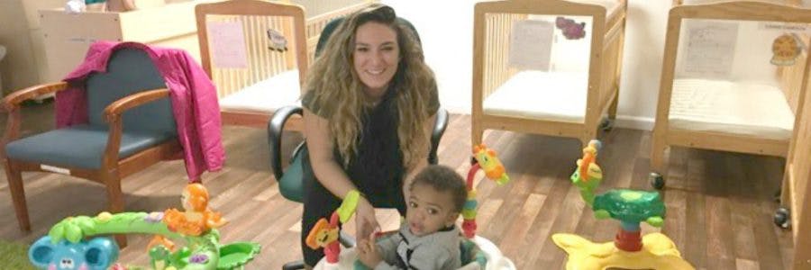 Person kneeling next to a child in a baby walker