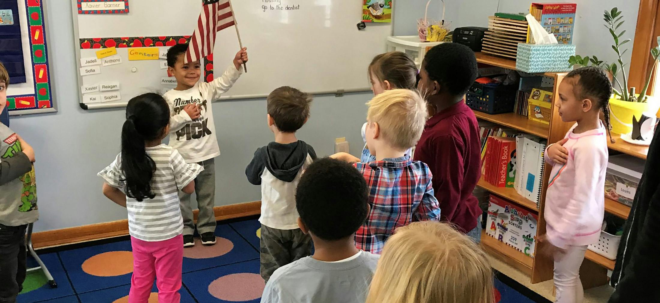 Child holding an American flag in front of other children in a classroom