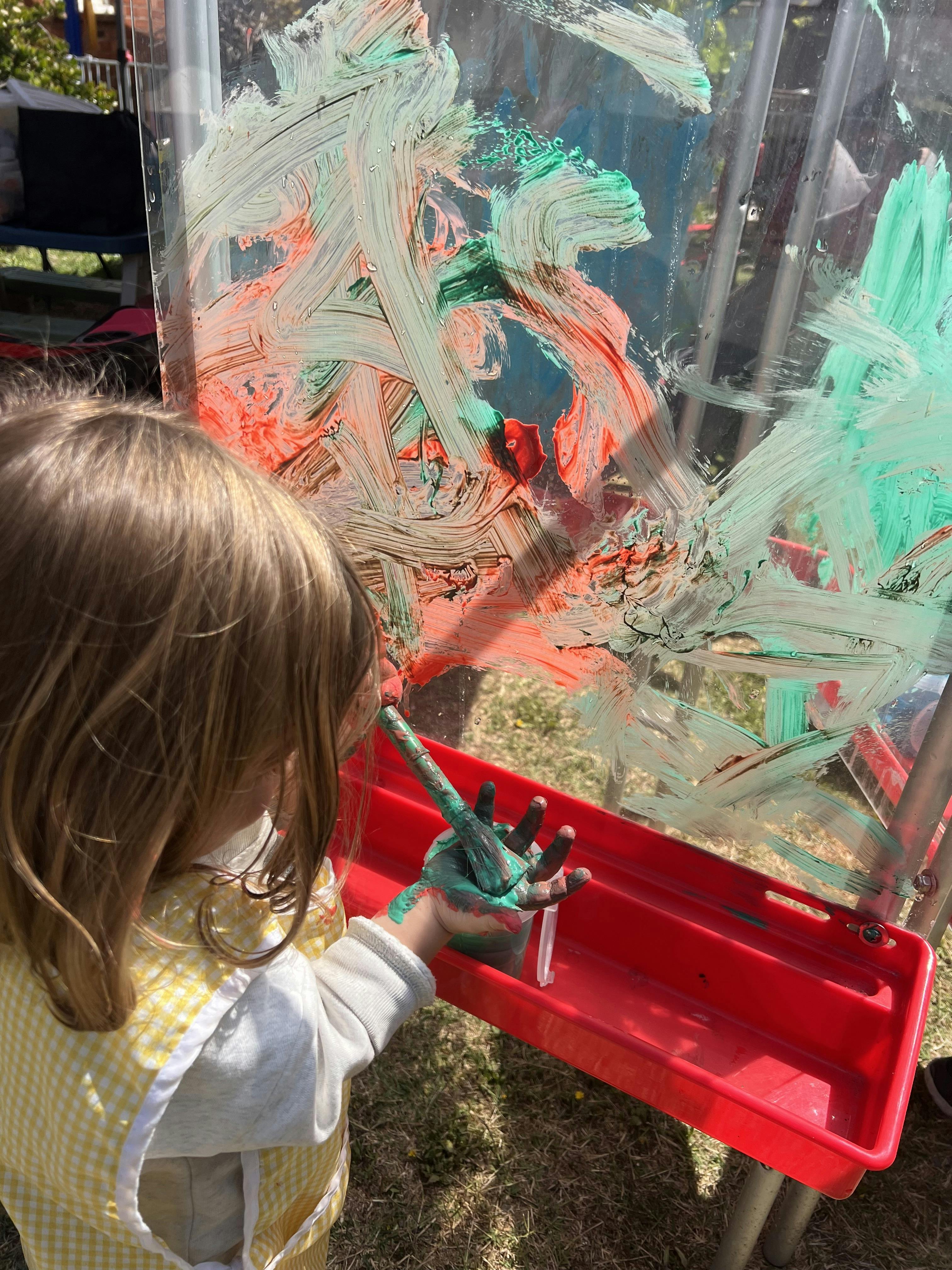 Child painting on a clear easel with green and orange paint