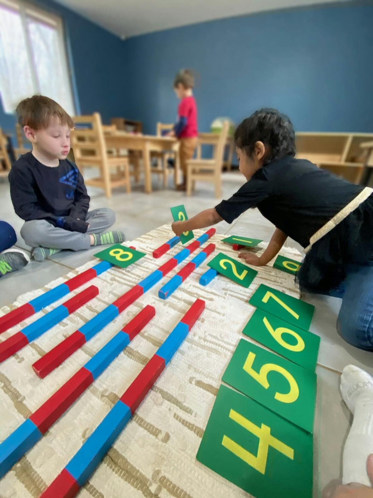 Child playing with number cards and counting rods on the floor