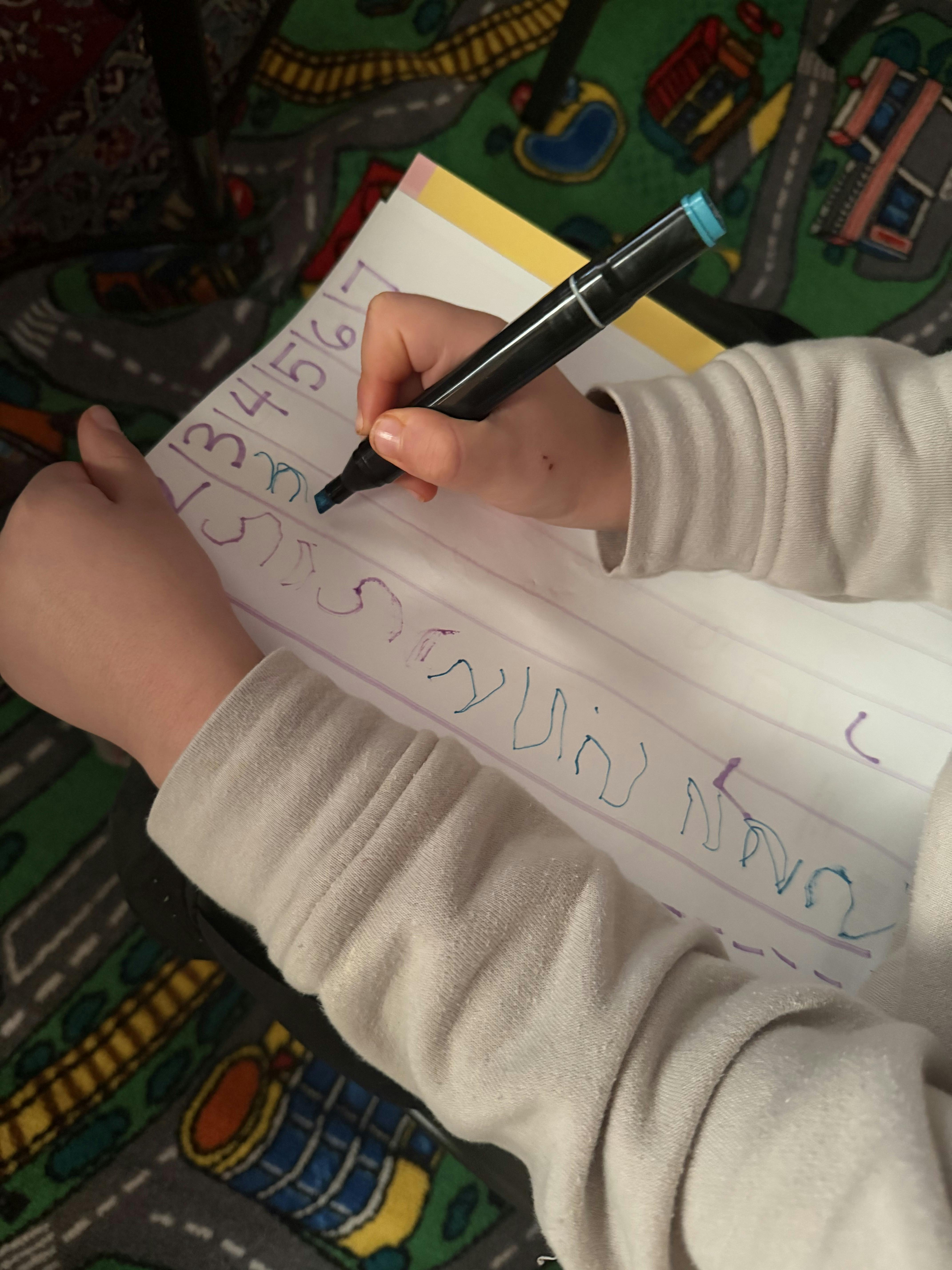 Child's hands writing numbers and letters on a paper with a blue marker