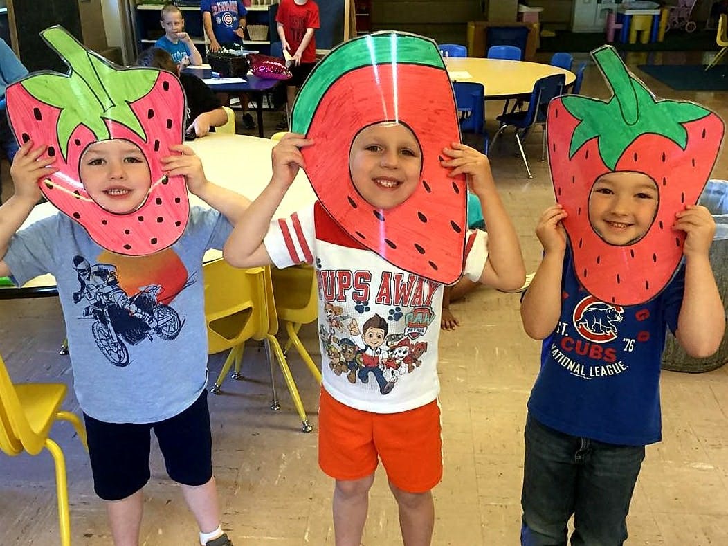 Three children holding up fruit cutouts to their faces