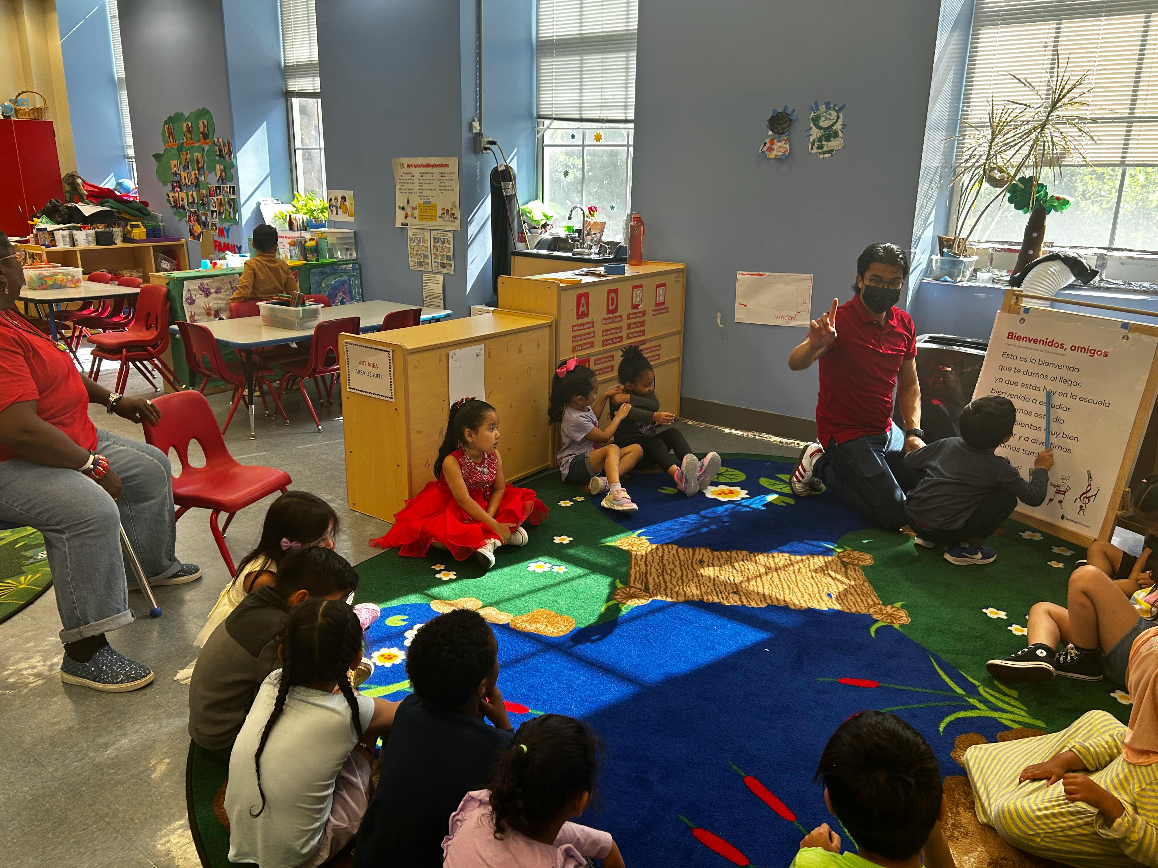 Adults and children in a classroom, some sitting on the floor, some at tables