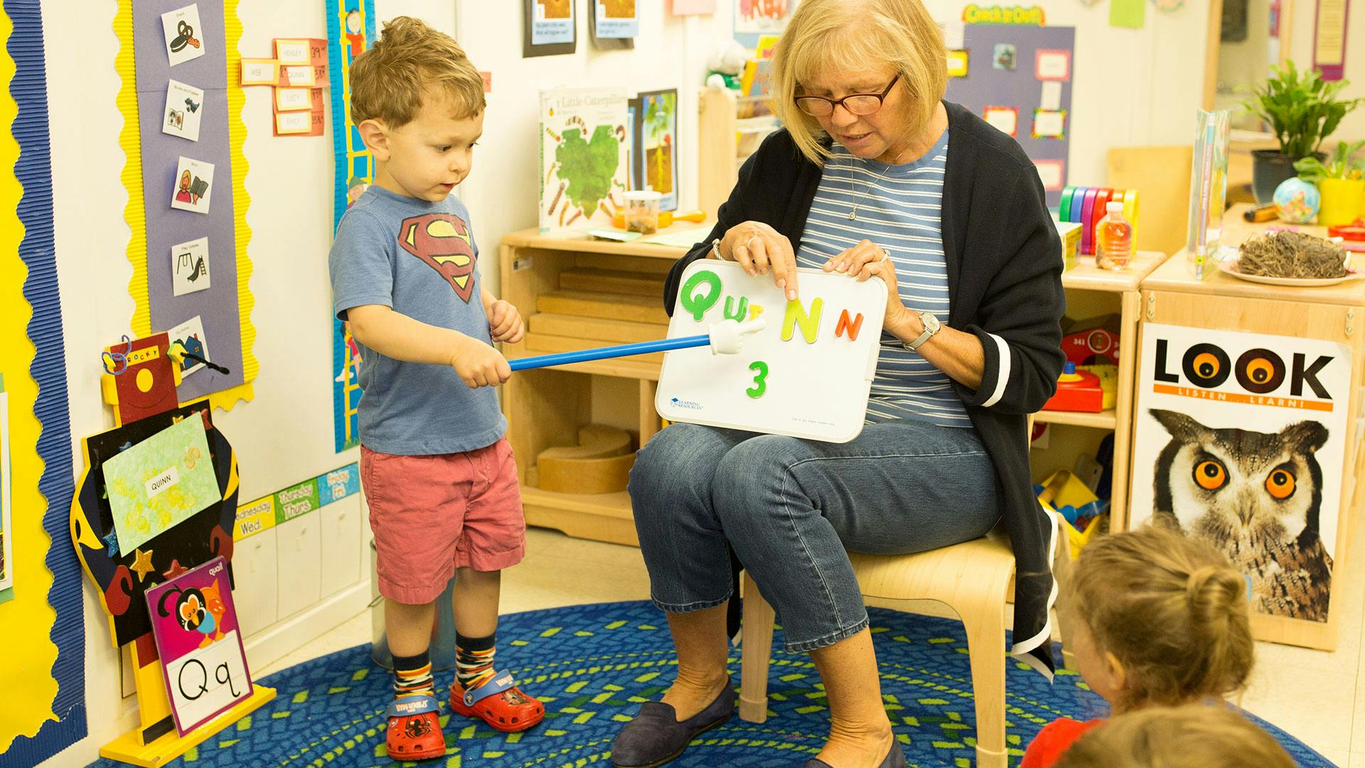 Adult and child pointing at a board with letters and numbers in a classroom