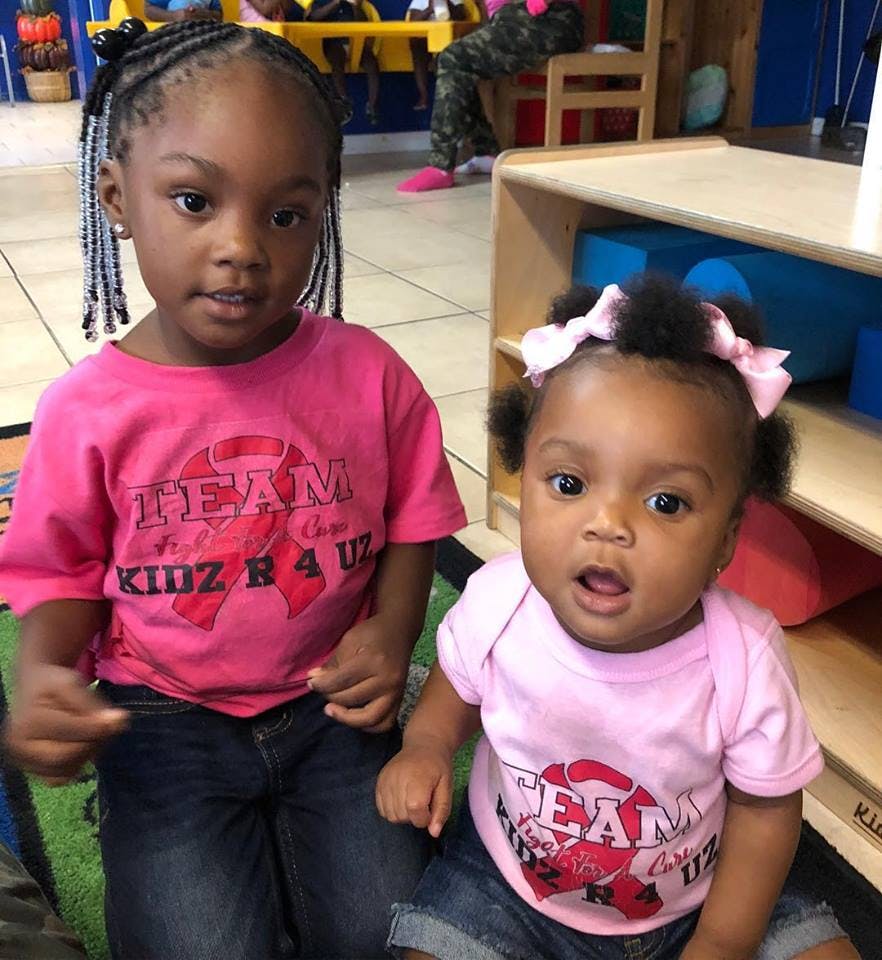 Child and baby wearing pink shirts with "TEAM KIDZ R 4 UZ" text
