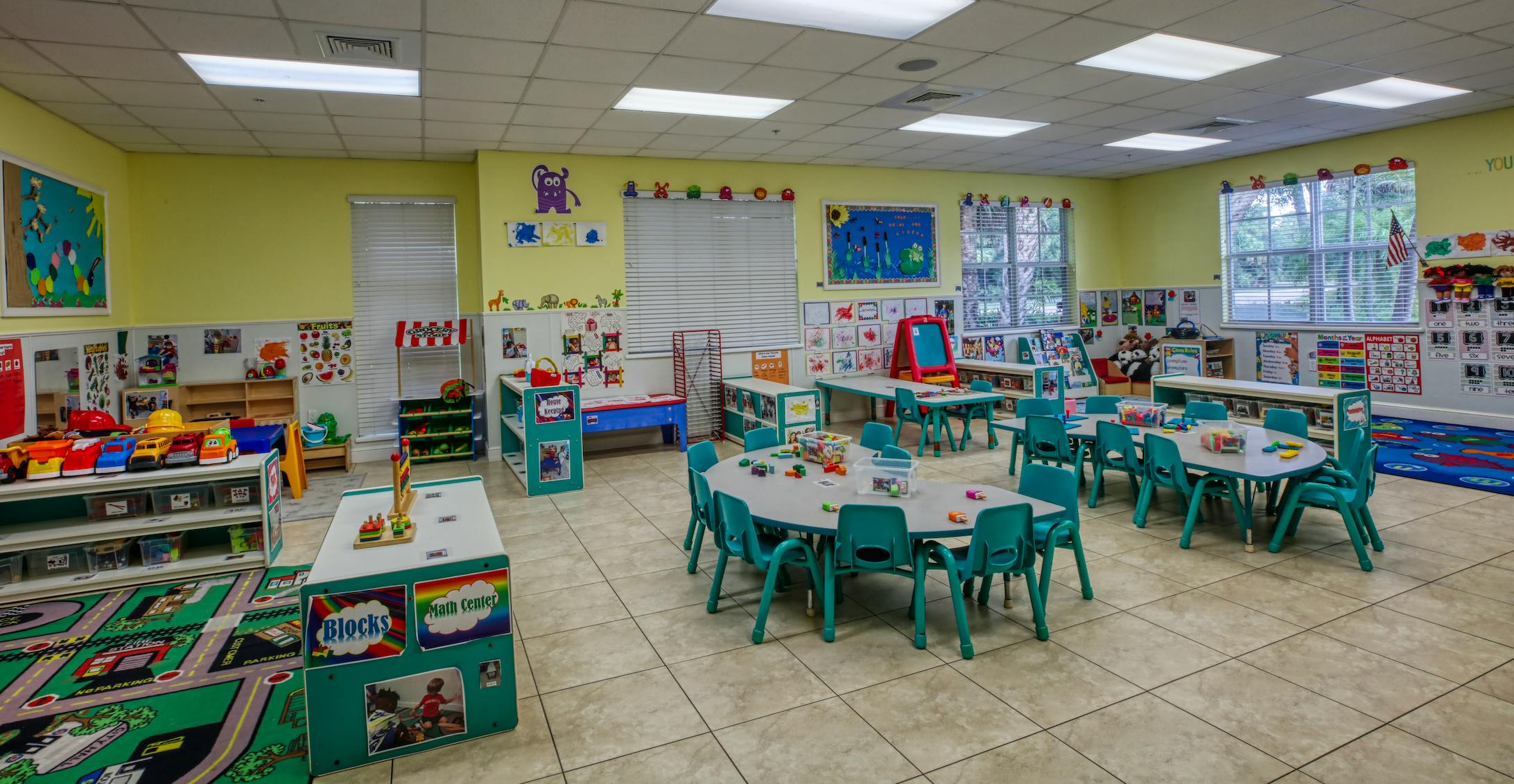 Colorful classroom with child-sized tables and chairs, toys, and educational posters