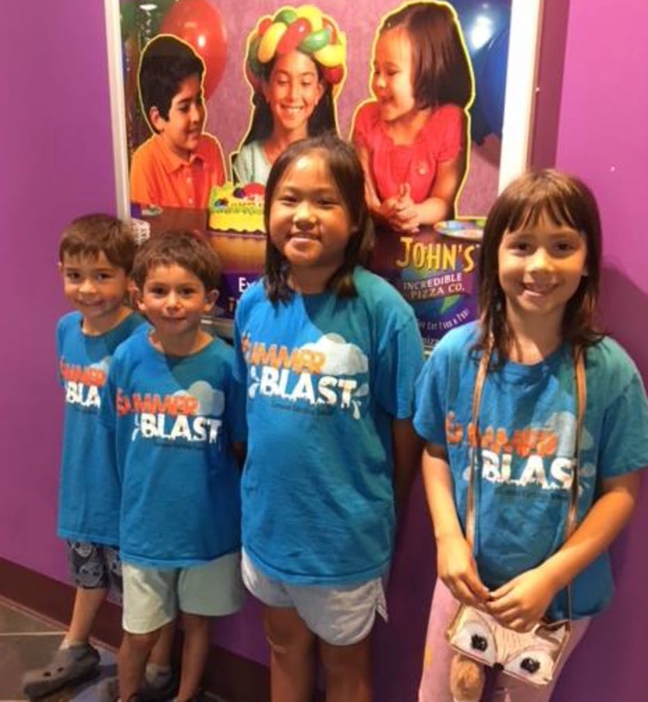 Four children in blue shirts standing in front of a poster