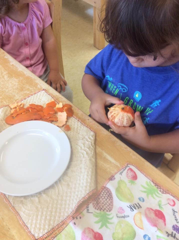 Child peeling an orange at a table
