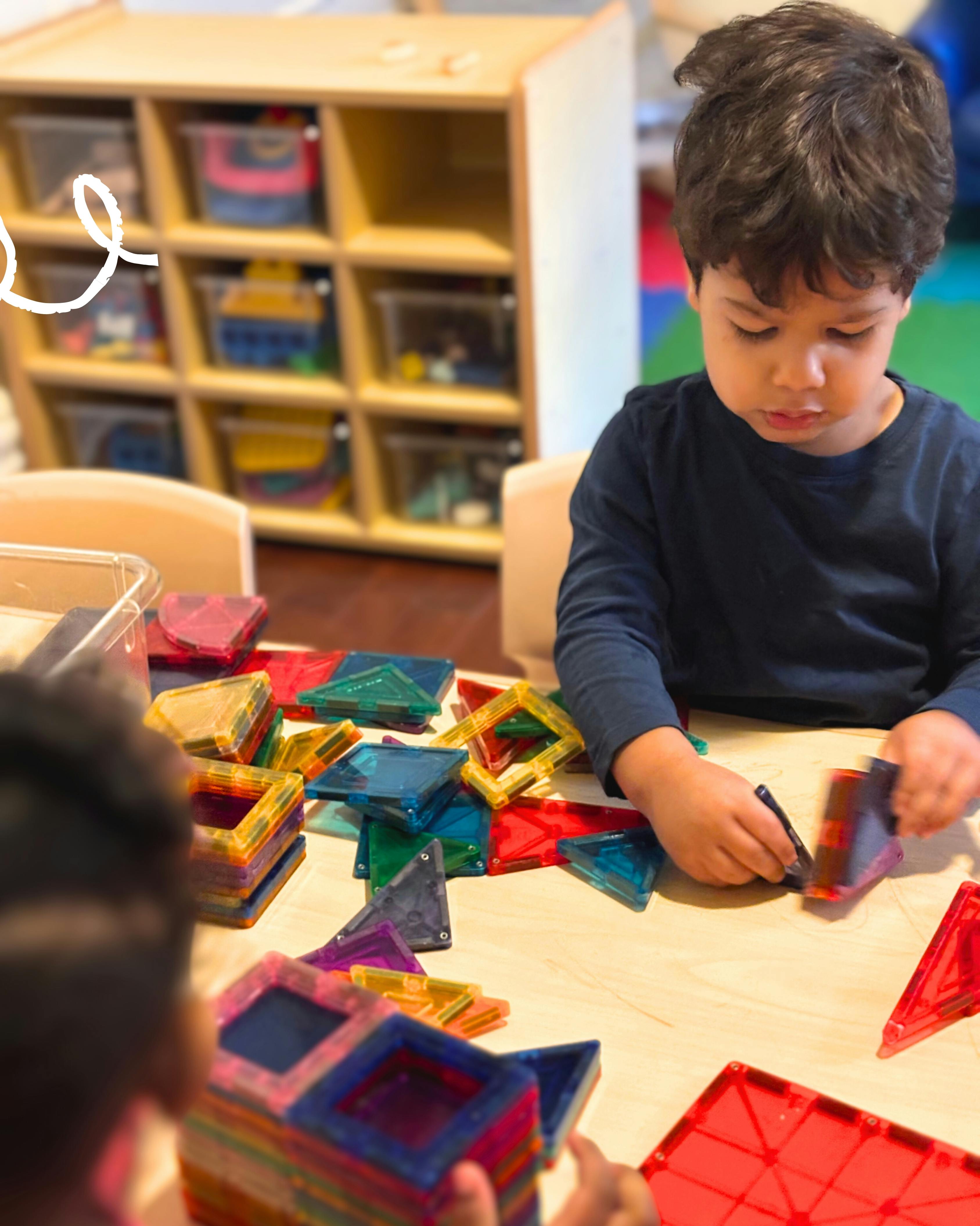 Child playing with colorful magnetic tiles at a table
