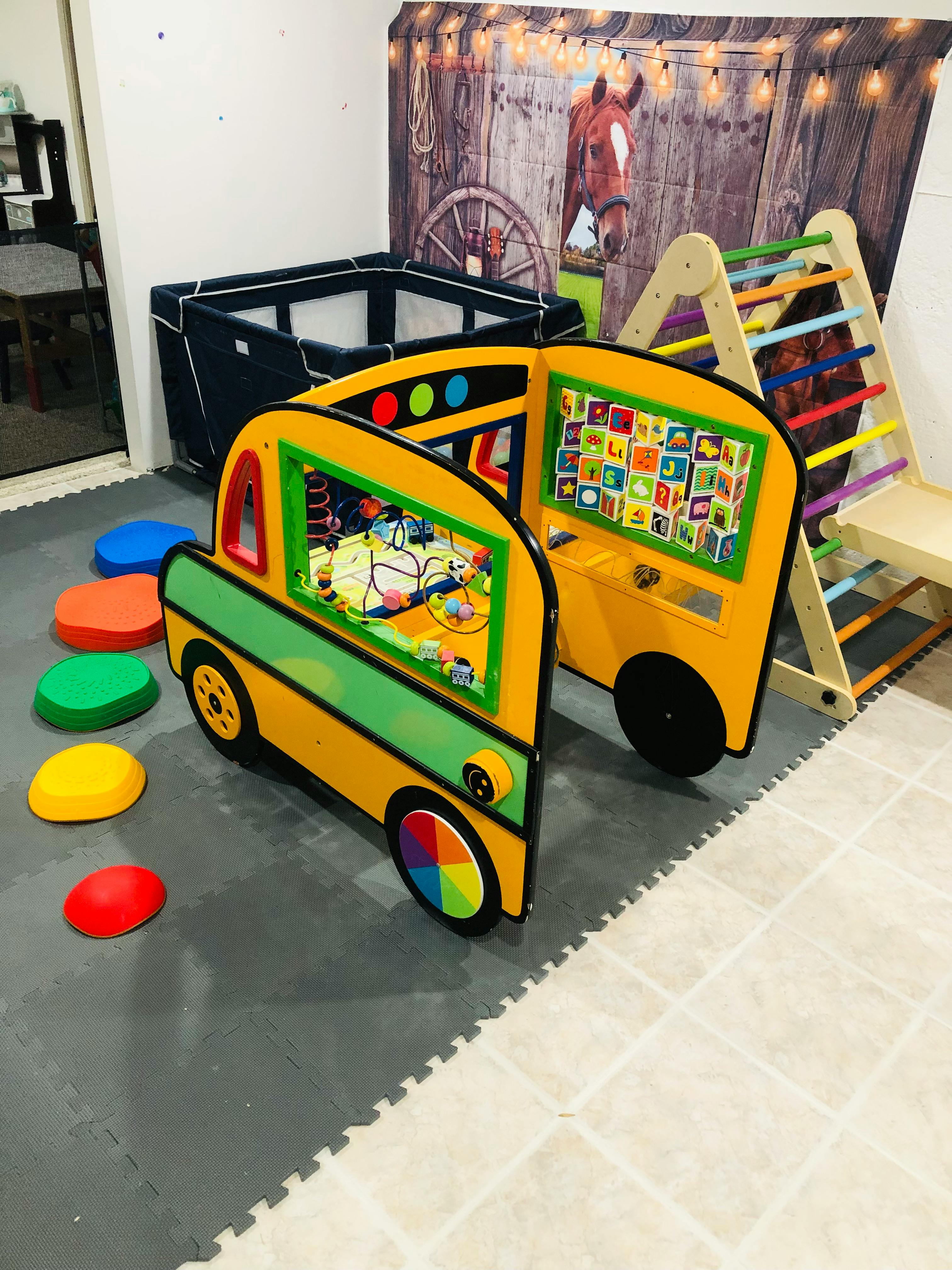Playroom with a yellow and green toy bus, colorful stepping stones, and a climbing frame