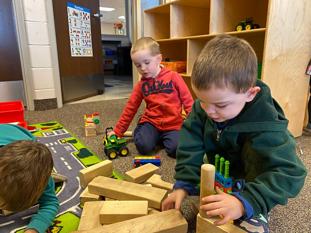 Two children playing with blocks and toy trucks on a rug
