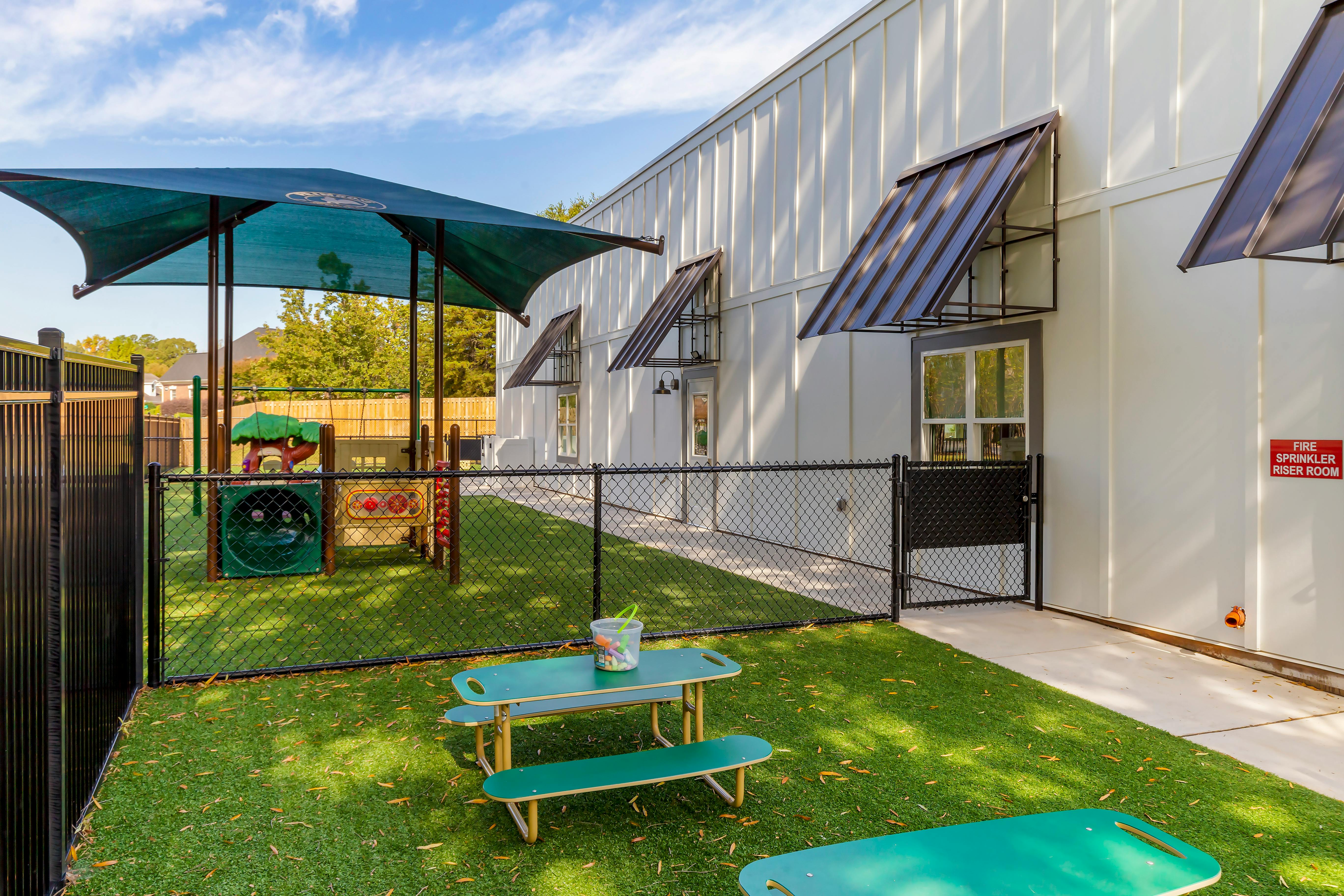 Playground area with a fenced-in play structure, canopy, and small picnic table