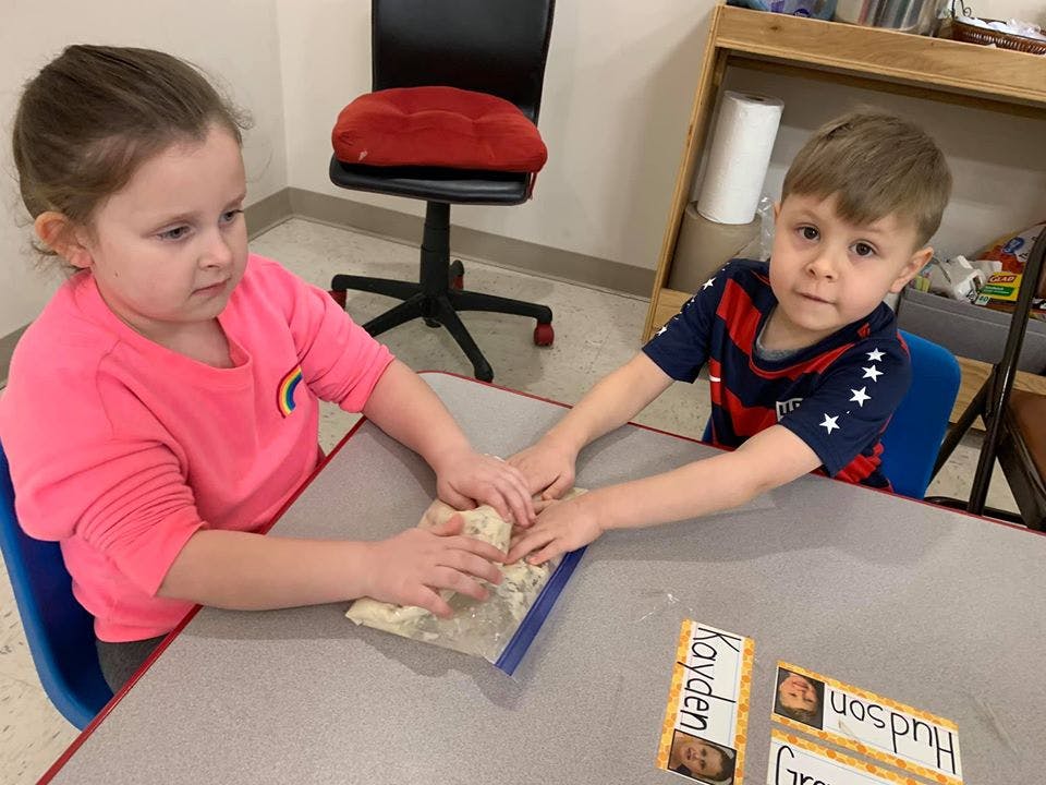 Two children playing with dough in a plastic bag at a table