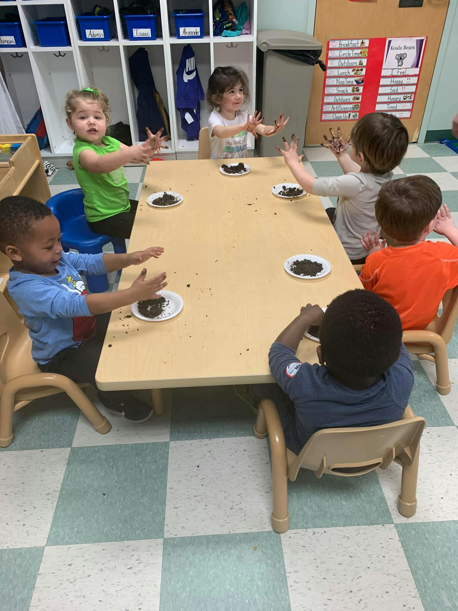 Children at a table with plates of dirt, some with dirty hands