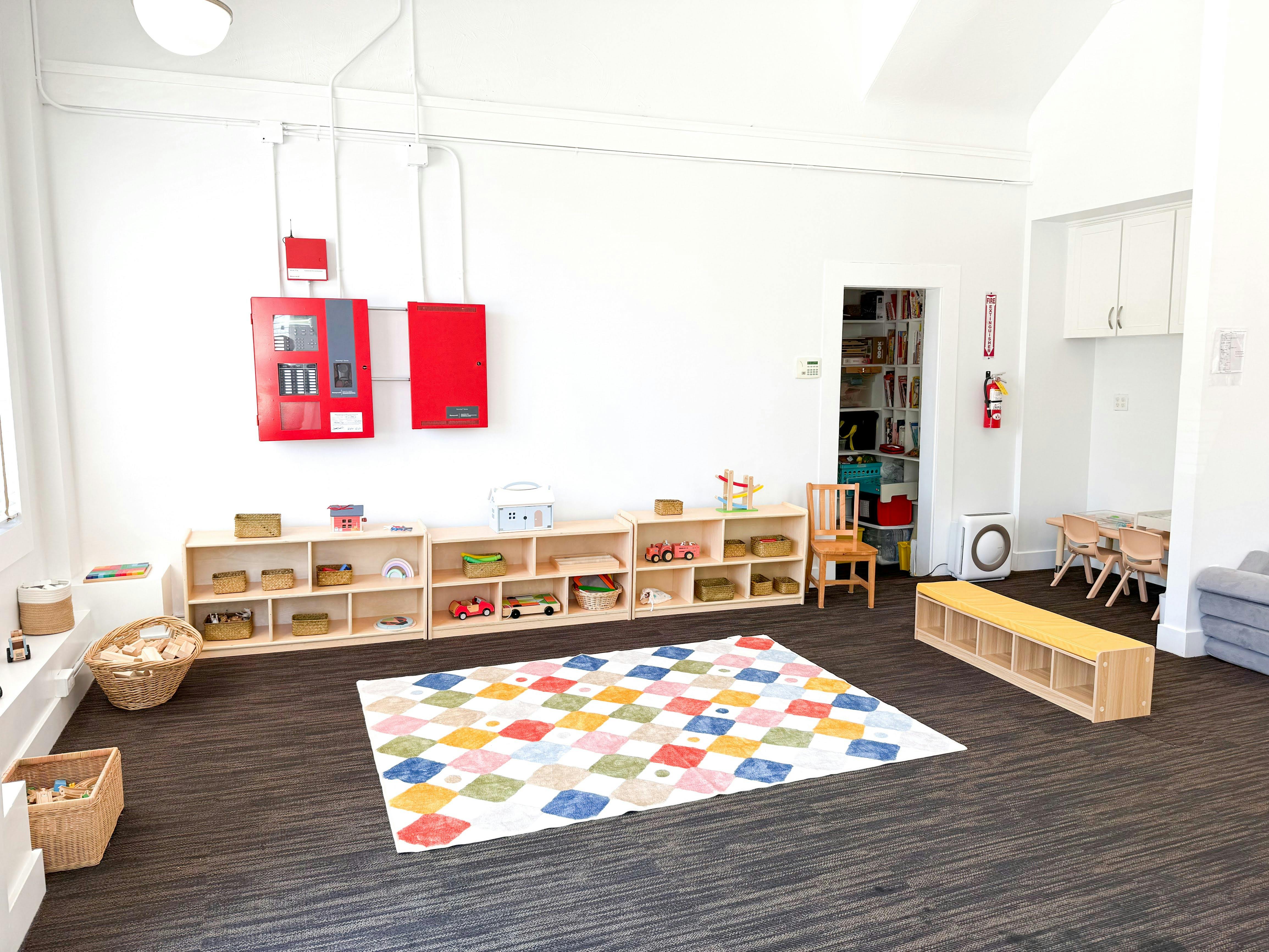 Childcare room with wooden shelves containing toys and a colorful patterned rug