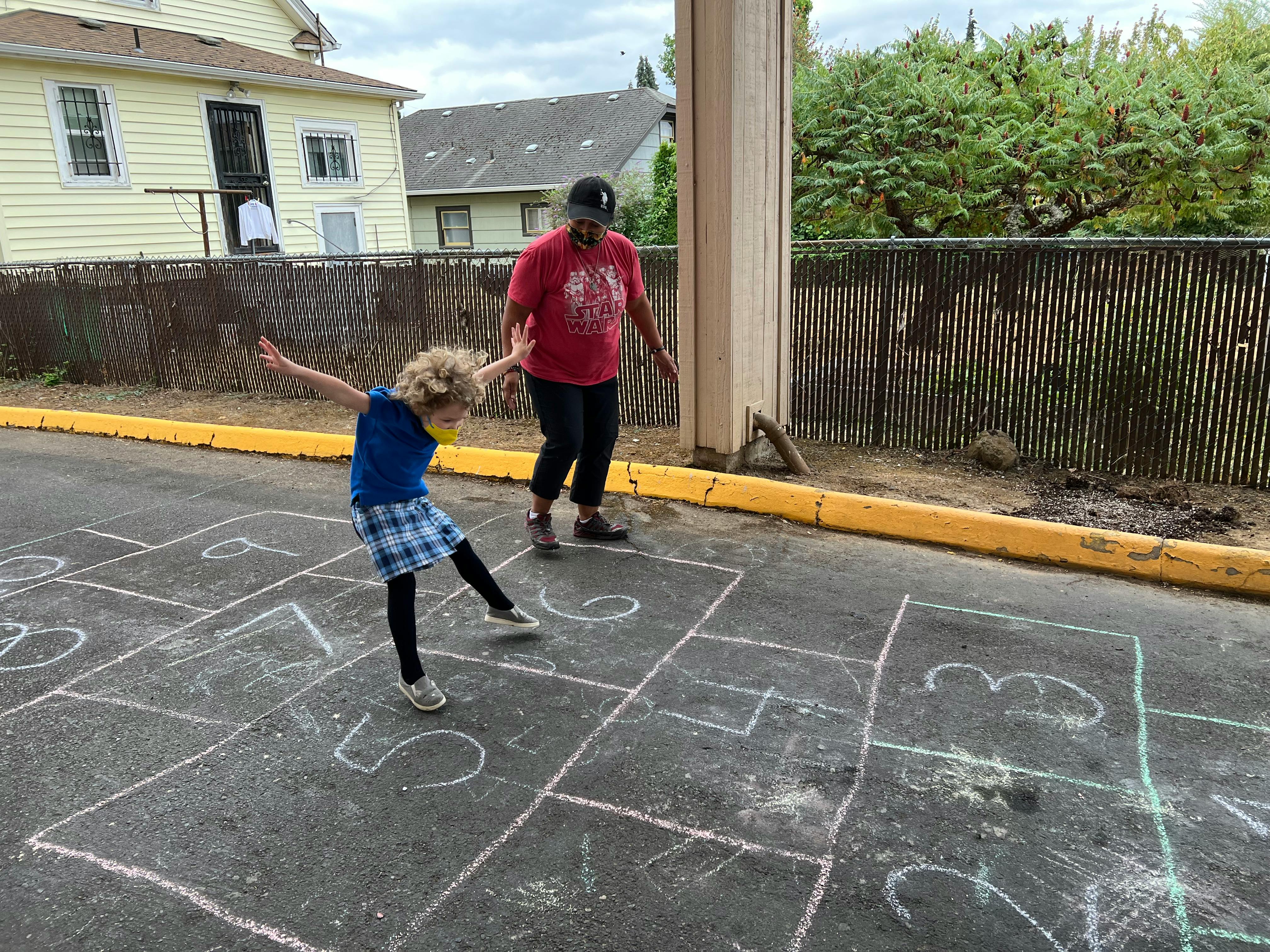 Child and person playing hopscotch on asphalt