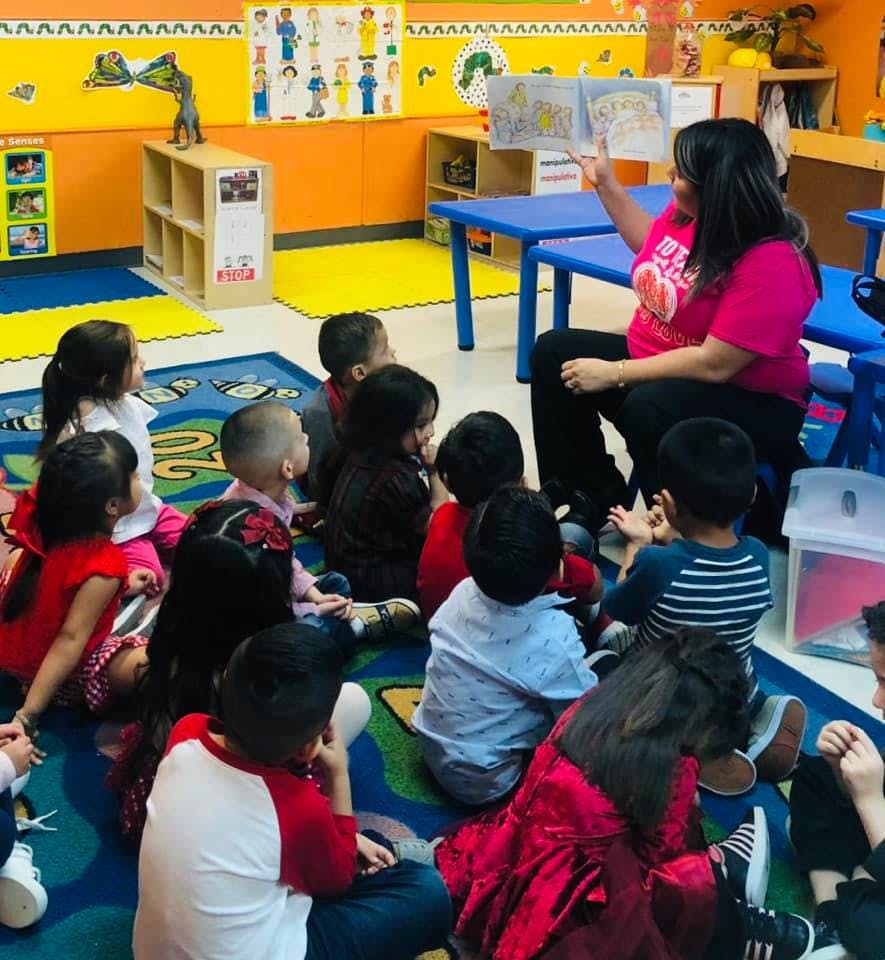 Person reading a book to a group of children in a classroom
