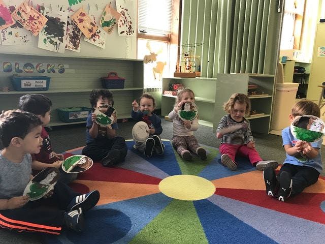 Children sitting on a colorful rug holding paper plates