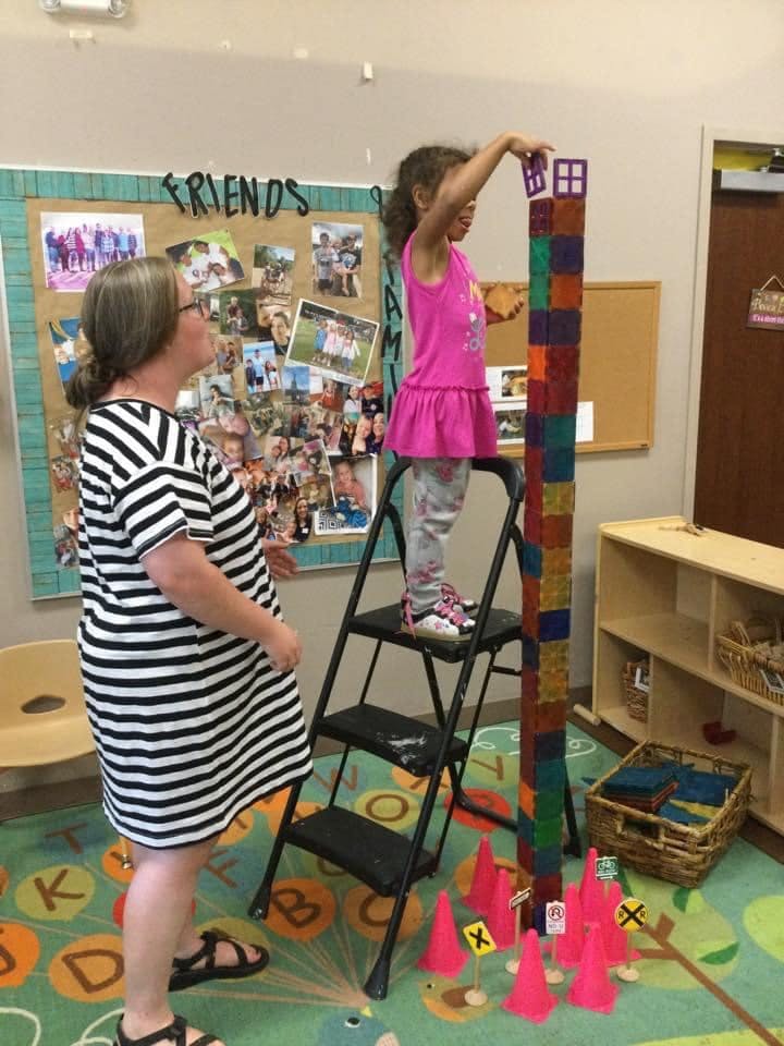 Adult and child building a tall tower with blocks in a classroom