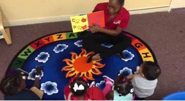 Person reading a book to children on a rug