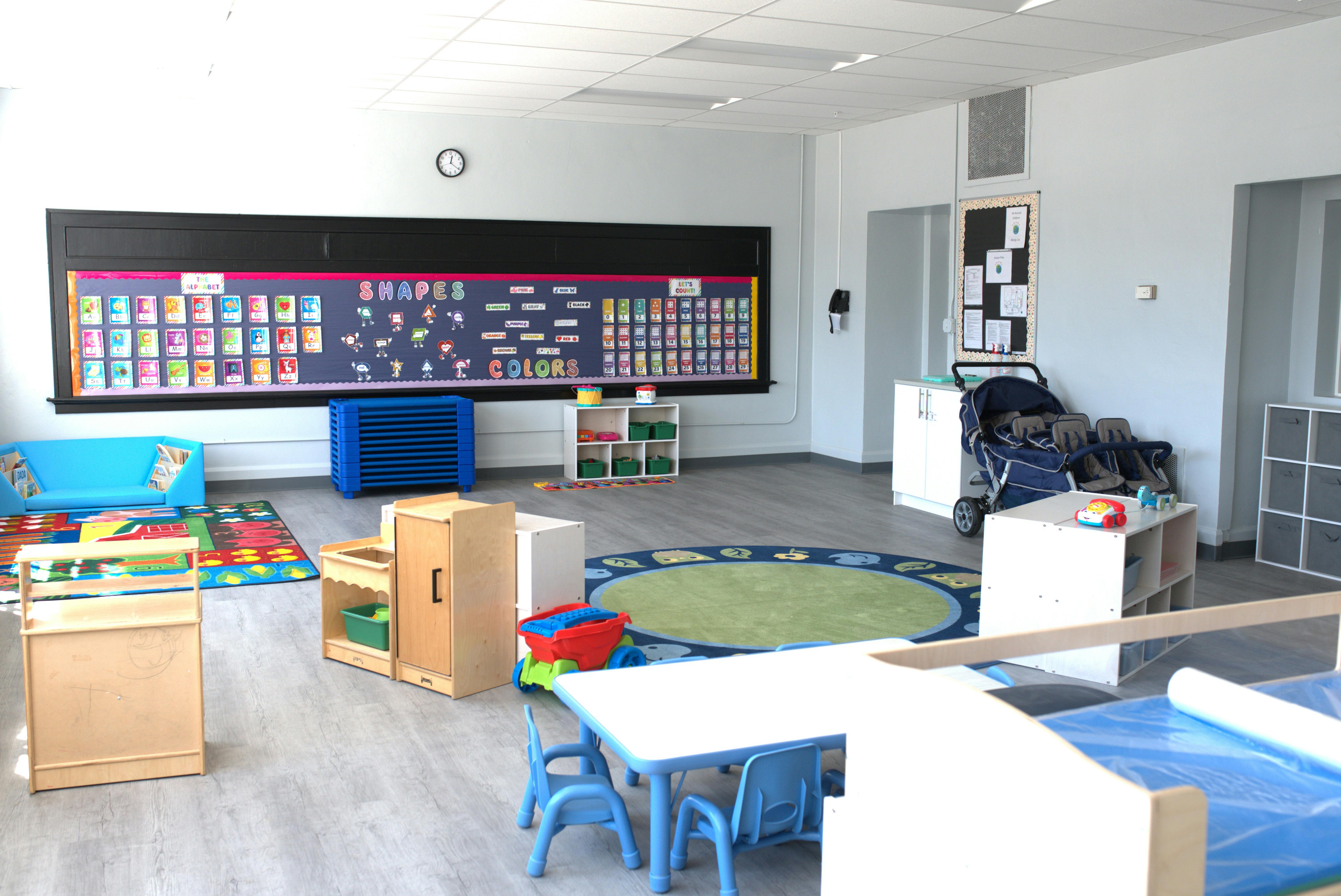 Classroom with a large bulletin board, small tables, and play mats