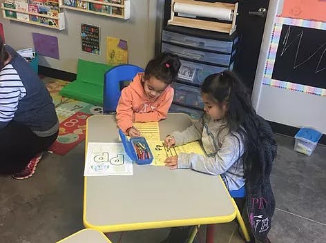 Two children drawing at a table in a classroom