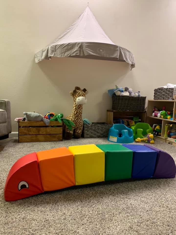 Rainbow caterpillar soft play toy on a carpeted floor in a playroom