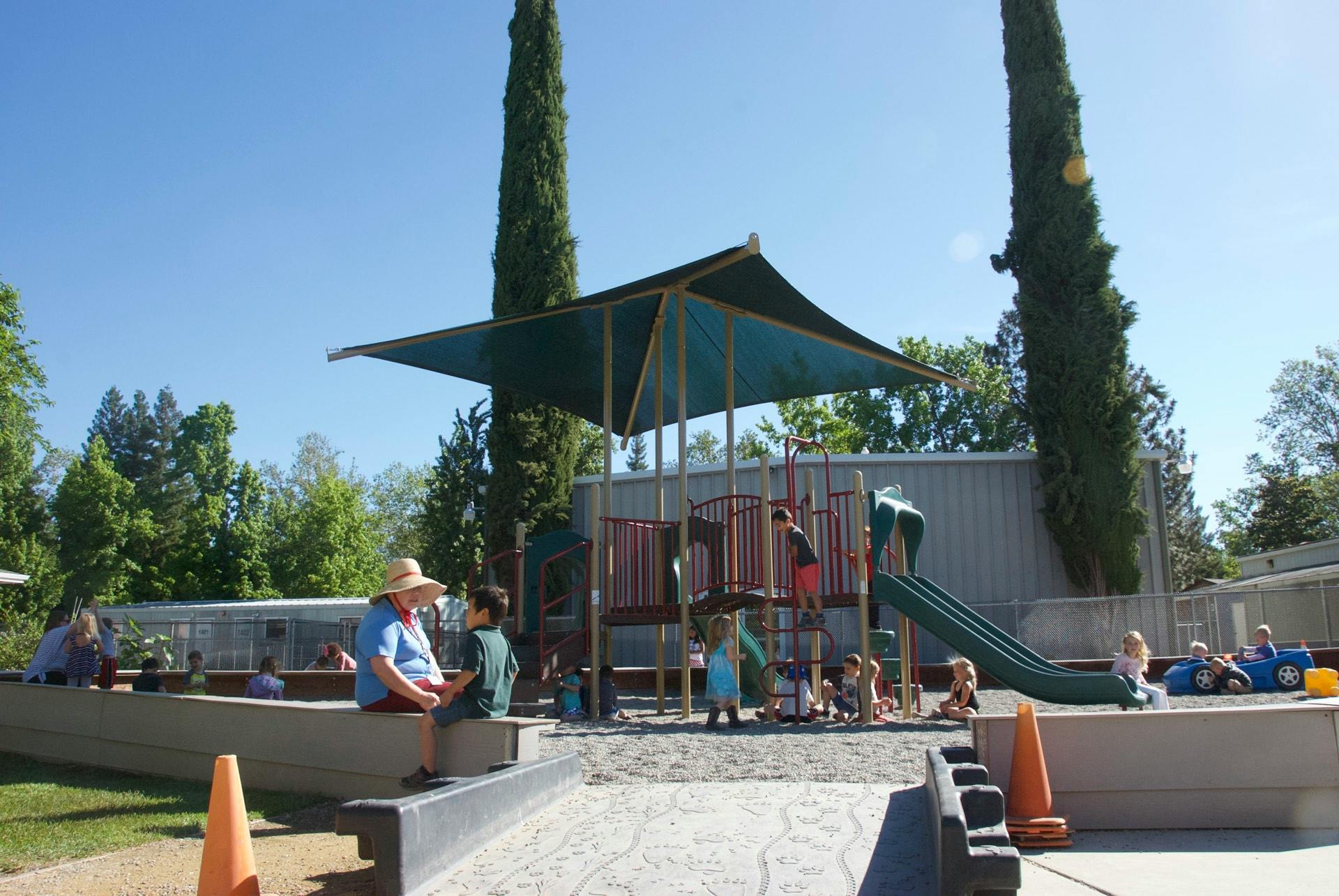 People and children on a playground with play structures and a slide