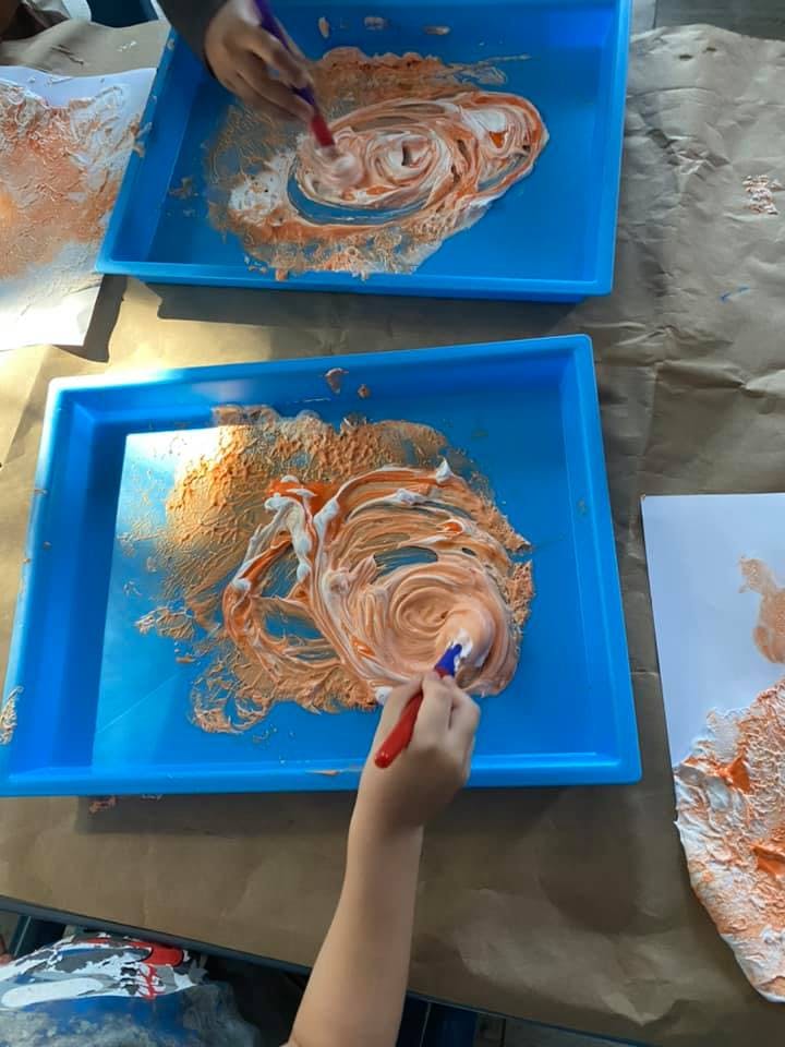 People painting with orange and white paint in blue trays