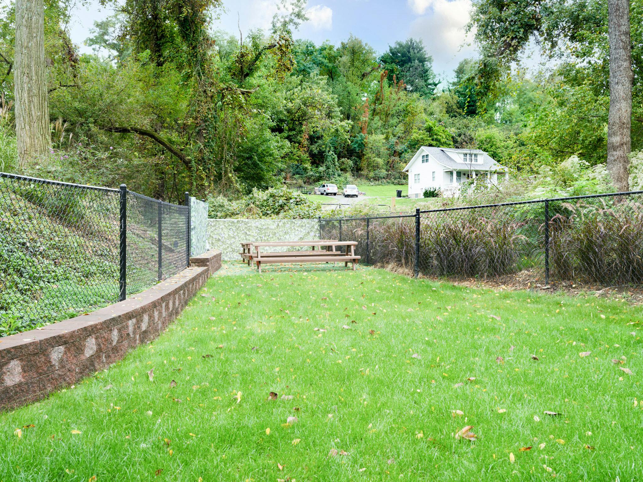 Grassy yard with a picnic table, fence, and house in the background