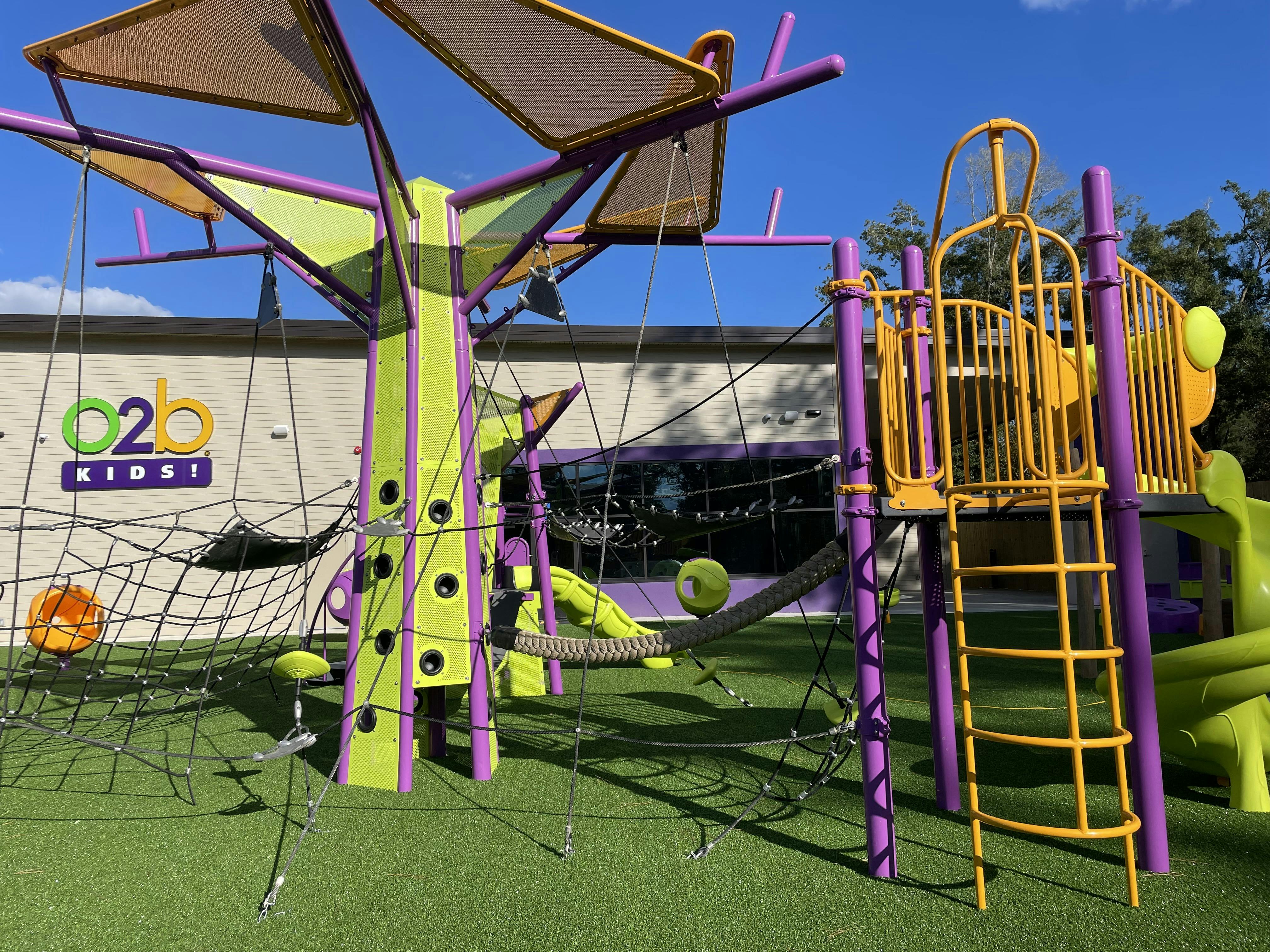 Colorful playground structure with climbing nets and slides on artificial turf