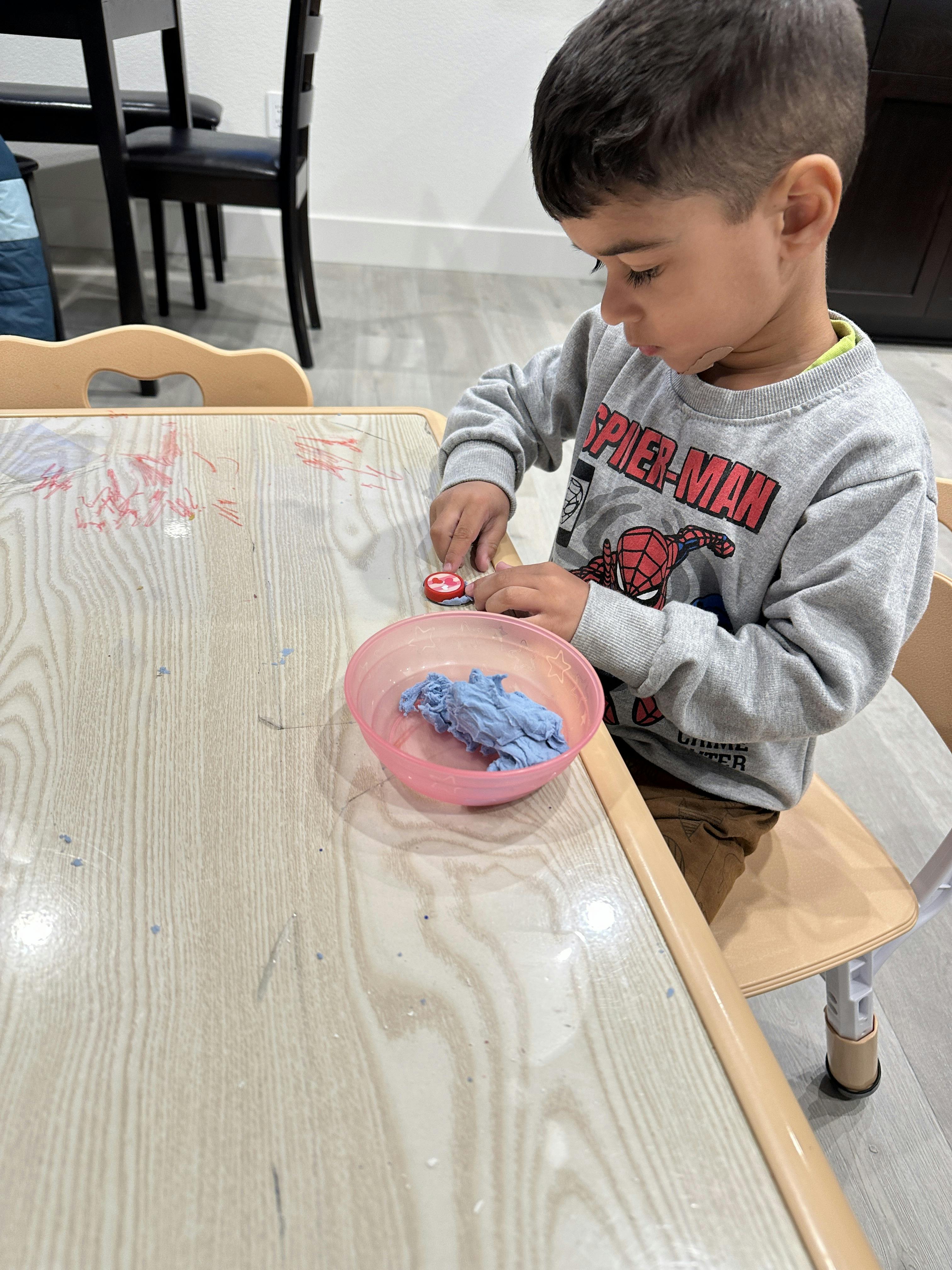 Child playing with a red toy and a pink bowl of blue kinetic sand at a table