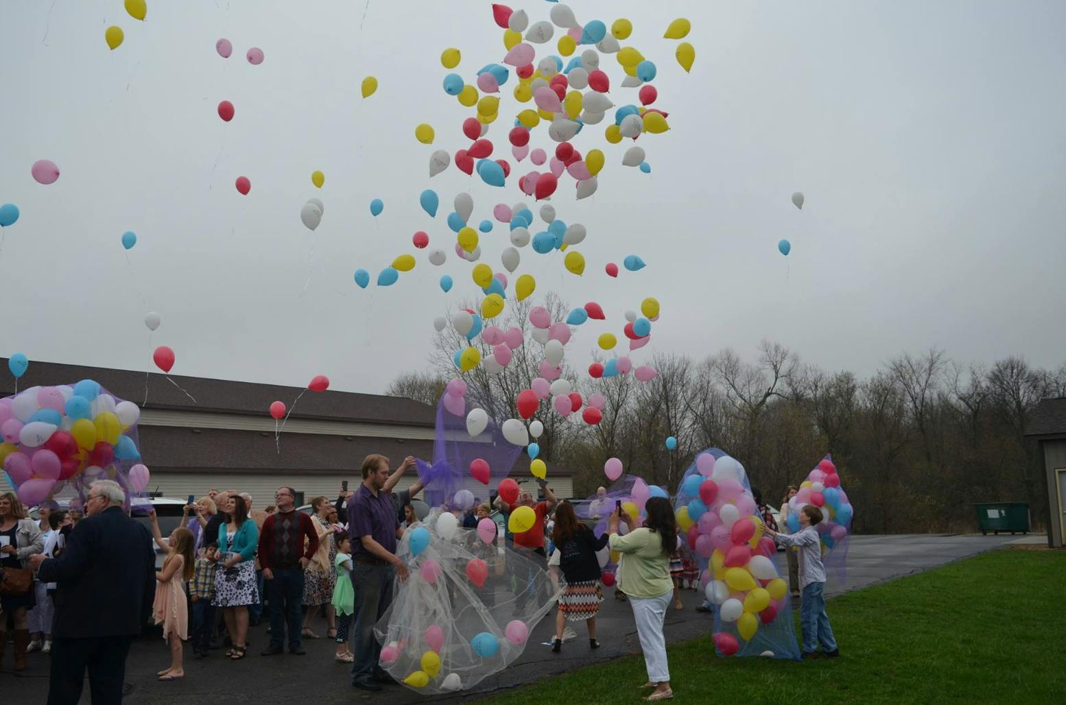 People releasing many colorful balloons into the sky outdoors
