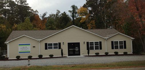 Single-story building with light-colored siding and dark shutters